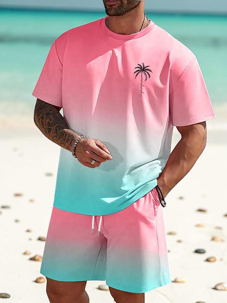 May include: A two-piece set featuring a pink and teal ombre design. The set includes a short-sleeved t-shirt with a palm tree graphic and matching shorts with a drawstring. The outfit is perfect for a beach day.