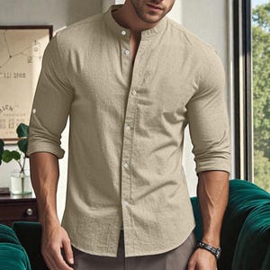 May include: A beige long-sleeve shirt with a mandarin collar and button-down front. The shirt has buttoned cuffs and is made of a lightweight fabric. The shirt is a casual style.