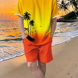 May include: A two-piece outfit featuring a yellow and orange gradient t-shirt with a palm tree graphic and orange shorts. The t-shirt has white trim on the sleeves and collar. The outfit is worn on a sandy beach with a sunset backdrop.
