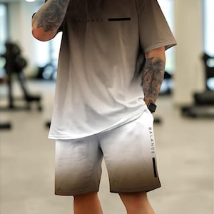 May include: A two-piece athletic set in a brown to white gradient. The short-sleeved top has "BALANCE" printed on the chest. The matching shorts also feature the word "BALANCE" on the side. The set is made of a lightweight, breathable fabric.