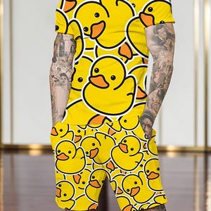 May include: Yellow matching t-shirt and shorts set featuring a repeating pattern of cartoon rubber ducks. The ducks have black outlines, orange beaks, and black eyes. The set is made of a lightweight material.