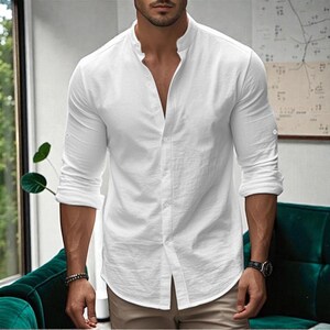 May include: White long-sleeve shirt with a mandarin collar and button-down front. The shirt has rolled-up sleeves and is made of a lightweight fabric. The shirt is paired with khaki-colored pants.