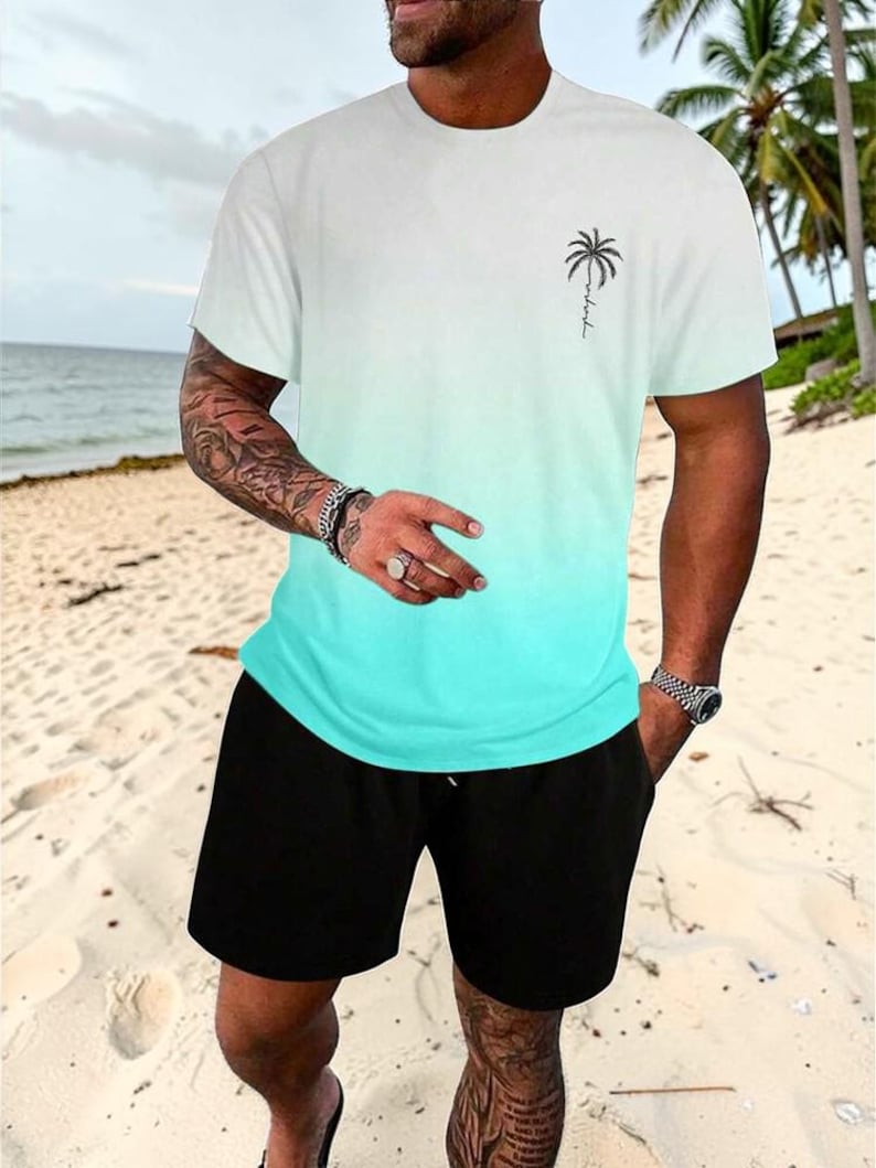 May include: White and turquoise ombre t-shirt with a palm tree graphic and black shorts. The t-shirt has a crew neck and short sleeves. The shorts are knee-length and have a drawstring waist. The outfit is worn on a sandy beach.