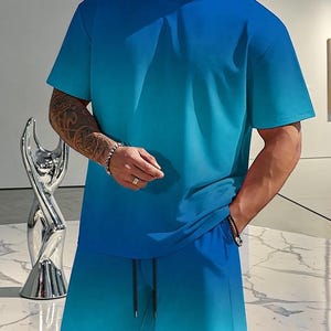 May include: A two-piece matching set in a blue gradient. The set includes a short-sleeved crew neck t-shirt and matching shorts with a drawstring. The color transitions from a darker blue at the top to a lighter blue at the bottom.