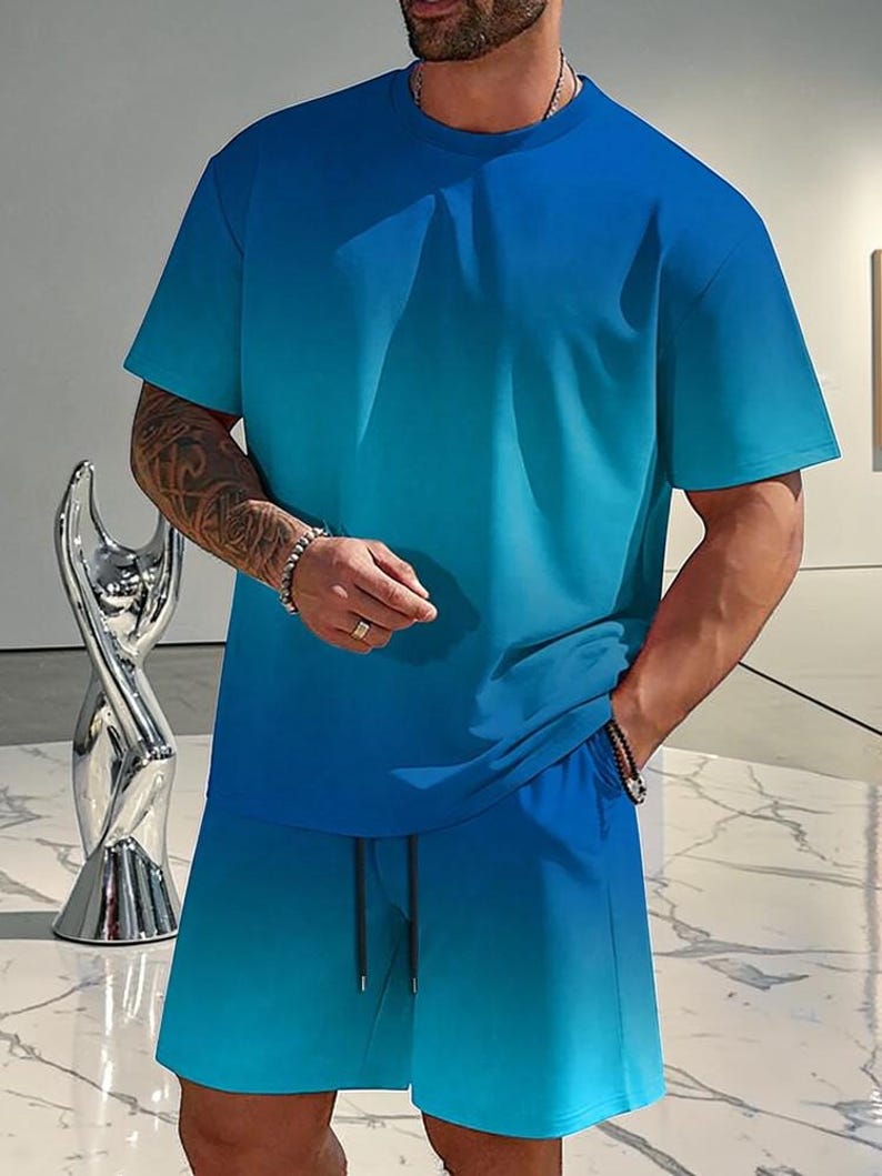 May include: A two-piece matching set in a blue gradient. The set includes a short-sleeved crew neck t-shirt and matching shorts with a drawstring. The color transitions from a darker blue at the top to a lighter blue at the bottom.