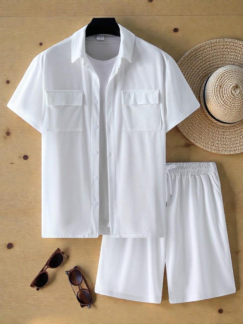 May include: A white short-sleeved shirt and shorts set with two chest pockets. The outfit is paired with a straw hat and two pairs of sunglasses. The clothing is made of a lightweight fabric, perfect for warm weather.