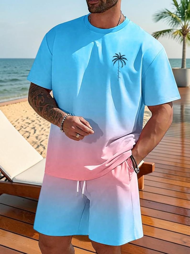 May include: A two-piece outfit featuring a blue and pink ombre design. The set includes a short-sleeved t-shirt with a palm tree graphic and matching shorts with a drawstring. The outfit is casual and suitable for warm weather.