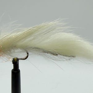 May include: A handmade fishing fly with a white, fluffy body and a yellow head. The fly is tied with various materials, including feathers and synthetic fibers, and features a curved hook. The fly is designed to mimic an insect or small baitfish.
