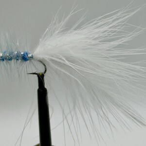 May include: A handmade fishing fly with a white feather tail and a blue and silver body. The fly is attached to a black hook and is designed for fly fishing. The fly is a popular choice for catching trout and other freshwater fish.