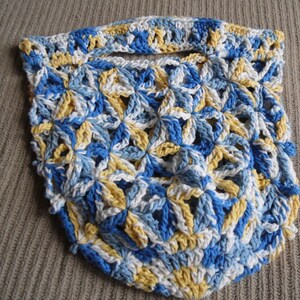 May include: A handmade crochet bag in a floral pattern. The bag features a combination of blue, white, and yellow yarn. The open weave design includes a handle at the top. The bag is likely used for carrying items.