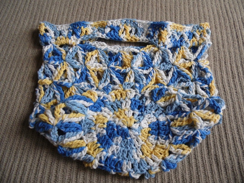 May include: Handmade crochet bag in a floral pattern. The bag features a handle and is made with blue, white, and yellow yarn. The bag is a unique accessory for carrying small items.