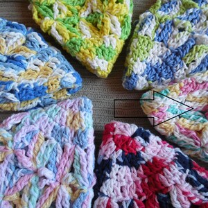 May include: A collection of colorful, handmade crochet washcloths. Each washcloth features a unique combination of pastel colors, including blue, yellow, pink, and green. The crochet pattern creates a textured, floral-like design.
