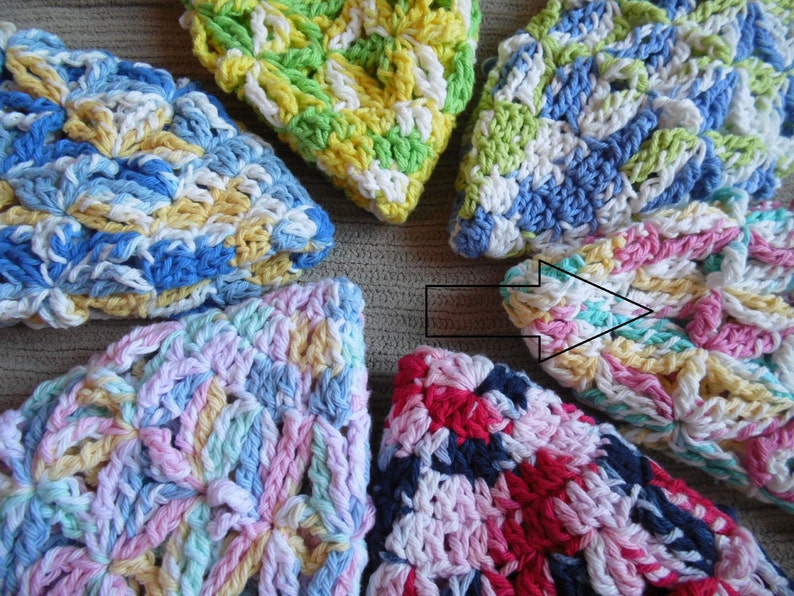 May include: A collection of colorful, handmade crochet washcloths. Each washcloth features a unique combination of pastel colors, including blue, yellow, pink, and green. The crochet pattern creates a textured, floral-like design.