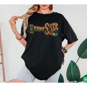 以下が含まれることがあります： TENNESSEEという文字がデザインされた黒の半袖Tシャツ。文字はギターの形にスタイライズされており、カウボーイブーツ、マイク、音符、夕暮れの風景のイメージが組み込まれています。