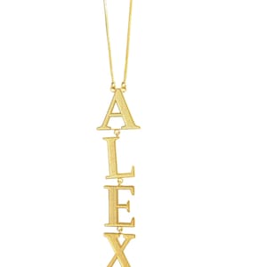 May include: A gold-coloured necklace spelling out the name "ALEX" vertically. The letters are linked and hang from a fine chain. The necklace is displayed against a white backdrop.