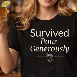 May include: Black t-shirt with the white text "Survived Pour Generously" and a cocktail graphic. The shirt is a crew neck style and appears to be made of a soft material. A person is holding a shot of liquor with a lime wedge.