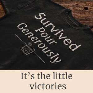 May include: Black t-shirt with the words "Survived Pour Generously" in white, along with a cocktail illustration. The phrase "It's the little victories" is printed below the shirt.