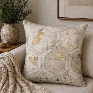 May include: A square throw pillow featuring a geometric hexagonal patchwork pattern in shades of cream, beige, and metallic gold. The surface displays a textured hide-like appearance with visible stitching and the text THE PILLOW ART HUB.