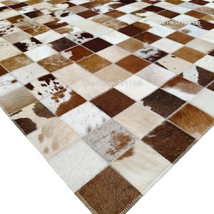 May include: A patchwork rug featuring a geometric design of squares in shades of brown, cream, and white. The rug is made from animal hide and has a stitched border. The Pillow Art Hub is printed on the rug.
