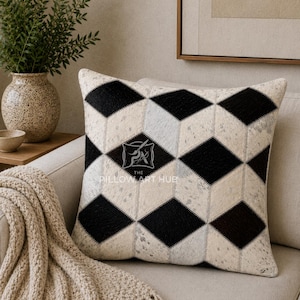 May include: A square throw pillow featuring a geometric pattern of black and off-white diamond shapes. The surface has a textured appearance with a visible logo in the centre that reads THE PILLOW ART HUB with a graphic icon of a paintbrush.