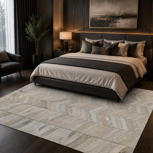 May include: A rectangular area rug featuring a repeating chevron pattern in shades of beige, cream, and light gray. The rug has a textured surface with subtle variations in tone and is positioned on a dark wood floor in a bedroom setting.