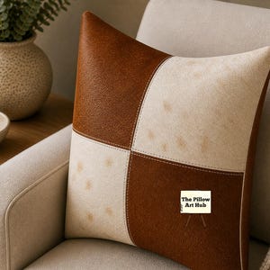 Può includere: Un cuscino quadrato decorativo con un design patchwork. Presenta due colori: marrone e bianco sporco. Le sezioni marroni hanno un aspetto strutturato, mentre le sezioni bianco sporco hanno un motivo maculato. Il cuscino è posto su una poltrona beige.