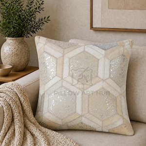 Könnte beinhalten: Ein quadratisches Zierkissen mit einem geometrischen Sechseck-Patchworkmuster in Beige-, Creme- und Metallic-Silbertönen. Die Oberfläche zeigt eine Mischung aus strukturierten Paneelen mit leichtem Glanz. Der Text PILLOW ART HUB ist mittig aufgedruckt.