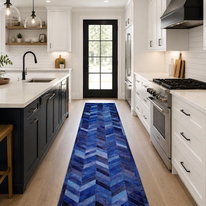 May include: A long, rectangular runner rug featuring a vibrant blue chevron pattern composed of stitched leather panels. The rug is positioned on a light-colored wooden floor in a kitchen setting, extending from the foreground toward a black door.