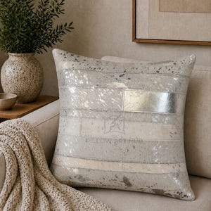 May include: A square throw pillow featuring a patchwork design of horizontal strips in metallic silver and light gray tones. The surface has a textured, hide-like appearance with a subtle sheen. The text PILLOW ART HUB is printed in the center.