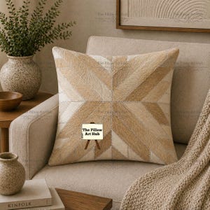 May include: A square decorative pillow with a geometric pattern in shades of beige and cream. The pillow is made of a patchwork of different textures and tones, creating a visually interesting design. It is placed on a beige armchair, with a neutral-toned throw blanket.