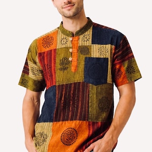 May include: A short-sleeved shirt featuring a patchwork design with various earth-toned squares in olive green, burnt orange, and navy blue. The shirt has a mandarin collar, a three-button placket with light-colored buttons, and a single chest pocket.