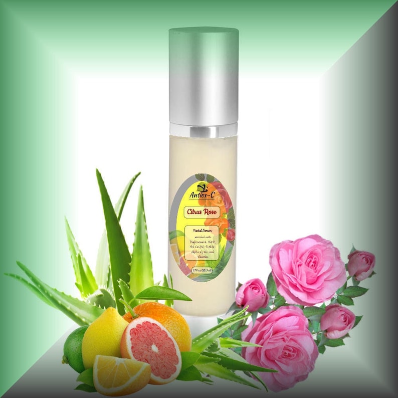 May include: A white bottle with a silver cap and a label that says "Antiox-C Citrus Rose Facial Serum". The bottle is surrounded by green aloe vera leaves, pink roses, and citrus fruits.