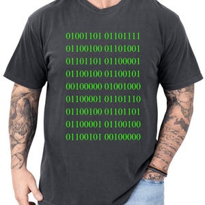 May include: Dark gray t-shirt with green binary code text. The text includes the numbers 0 and 1, arranged in rows. The shirt has a v-neck and short sleeves.