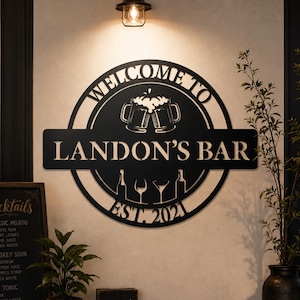 Puede incluir: Un letrero de pared circular de metal negro con el texto WELCOME TO LANDON'S BAR EST. 2021. El diseño incluye un gráfico de dos jarras de cerveza brindando en la parte superior y siluetas de dos botellas y dos tipos de copas en la parte inferior.