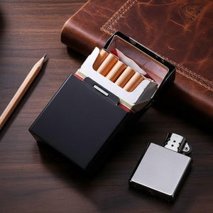 May include: A black cigarette case with a partially open pack of cigarettes, next to a silver lighter. The cigarettes are visible inside the white and gold-trimmed pack. A pencil and a leather-bound notebook are in the background.