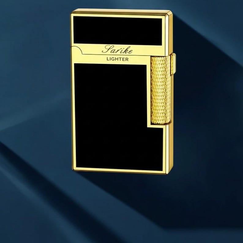 May include: A gold-coloured Sarike lighter with a black rectangular panel and a textured gold roller. The lighter has the word "Sarike" and the word "Lighter" printed on it. The lighter is set against a dark blue background.