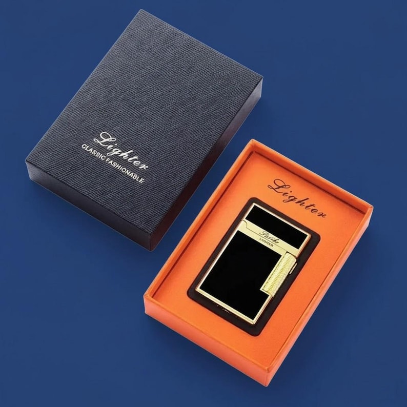 May include: A black and gold lighter in an orange box, with the word "Lighter" printed on the box. The lighter is rectangular with gold accents. The box is inside a dark blue box with the words "Lighter Classic Fashionable" printed on the lid.