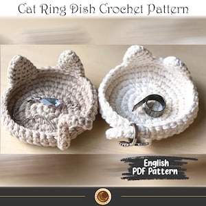 Könnte beinhalten: Zwei handgefertigte Ring-Schalen in Katzenform aus Häkelarbeit. Eine ist beige und enthält eine Halskette mit Anhänger. Die andere ist weiß, mit einem Metallring und einem Silberring. Der Text "Cat Ring Dish Crochet Pattern" steht oben.