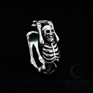 May include: A silver-toned metal ring featuring a detailed skeleton figure with arms raised above its head. The skeleton's ribcage and skull form the main decorative element of the band, which wraps around the finger in a continuous loop.
