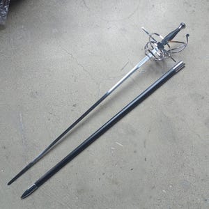 May include: A rapier sword with a long, slender, double-edged steel blade and a complex, polished silver-tone metal swept-hilt guard. The handle is black with a silver pommel. A matching black scabbard with silver-tone metal fittings is included.
