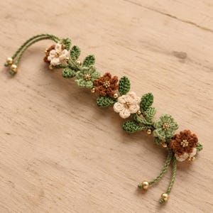 Pu&ograve; includere: Un braccialetto all'uncinetto con una serie di piccoli fiori color crema, verde chiaro e marrone, intervallati da foglie all'uncinetto verde scuro. Il motivo floreale &egrave; arricchito da minuscole perline dorate al centro e alle estremit&agrave;.