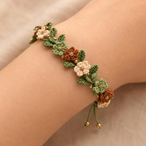 Pu&ograve; includere: Un braccialetto all'uncinetto con un design a tralcio di vite con piccole foglie verdi e fiori alternati nei colori crema, verde chiaro e marrone. Gli elementi floreali sono arricchiti da minuscole perline dorate e terminano con due sottili cordini verdi con perline dorate alle estremit&agrave;.