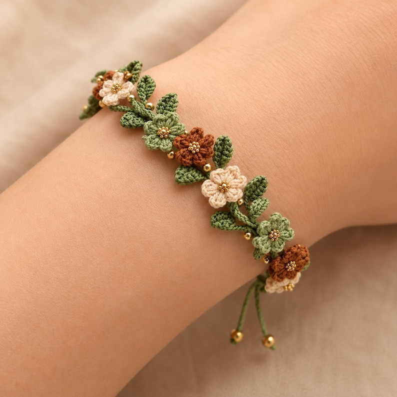 Pu&ograve; includere: Un braccialetto all'uncinetto con un design a tralcio di vite con piccole foglie verdi e fiori alternati nei colori crema, verde chiaro e marrone. Gli elementi floreali sono arricchiti da minuscole perline dorate e terminano con due sottili cordini verdi con perline dorate alle estremit&agrave;.