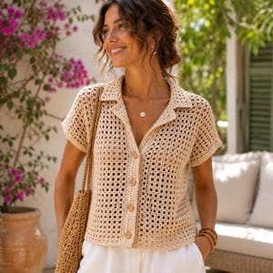May include: A beige short-sleeved button-down shirt featuring an open-knit crochet pattern with a classic collar. The garment is crafted with a square grid texture and includes four visible buttons down the front center, paired with a woven tote bag.