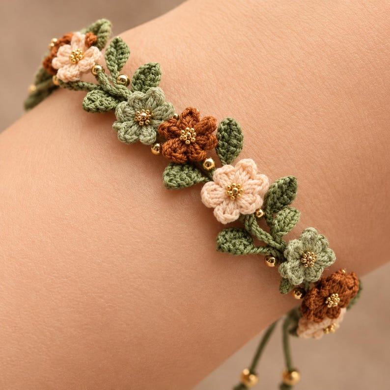 Pu&ograve; includere: Un braccialetto floreale con fiori all'uncinetto nei toni del crema, verde salvia e marrone ruggine, intervallati da piccole perline dorate metallizzate. Il design include foglie all'uncinetto verdi dettagliate e sottili cordini verdi.