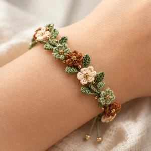 Pu&ograve; includere: Un braccialetto all'uncinetto con una serie di piccoli fiori a cinque petali nelle tonalit&agrave; crema, verde chiaro e marrone, intervallati da foglie all'uncinetto verdi e minuscole perline dorate. Il bracciale ha estremit&agrave; regolabili.