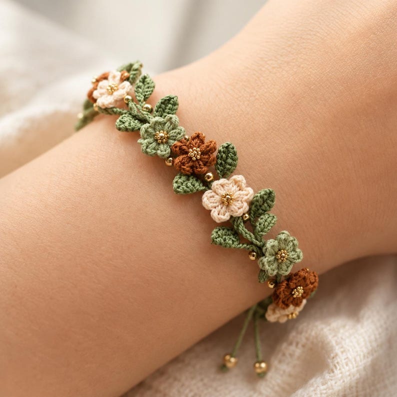 Pu&ograve; includere: Un braccialetto all'uncinetto con una serie di piccoli fiori a cinque petali nelle tonalit&agrave; crema, verde chiaro e marrone, intervallati da foglie all'uncinetto verdi e minuscole perline dorate. Il bracciale ha estremit&agrave; regolabili.