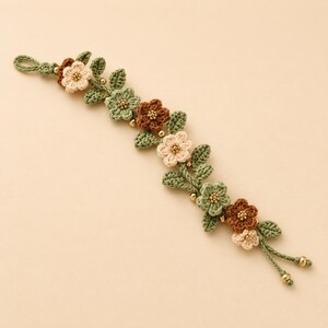Pu&ograve; includere: Un braccialetto all'uncinetto con un design a tralcio di vite con foglie verde salvia e piccoli fiori nelle tonalit&agrave; crema, verde chiaro e marrone. I centri dei fiori sono accentuati da minuscole perline dorate e le estremit&agrave; hanno perline.