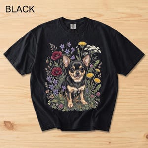 May include: Black t-shirt featuring a Chihuahua dog surrounded by colorful flowers. The dog is black and tan, with a happy expression. The flowers include red poppies, purple blooms, and yellow dandelions. The word "BLACK" is printed at the top.