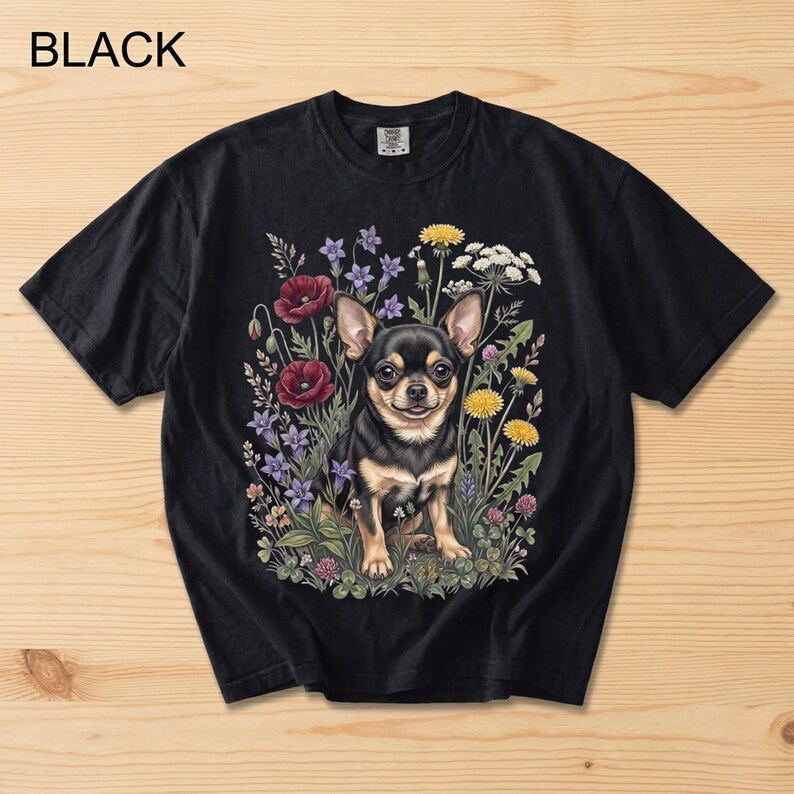 May include: Black t-shirt featuring a Chihuahua dog surrounded by colorful flowers. The dog is black and tan, with a happy expression. The flowers include red poppies, purple blooms, and yellow dandelions. The word "BLACK" is printed at the top.